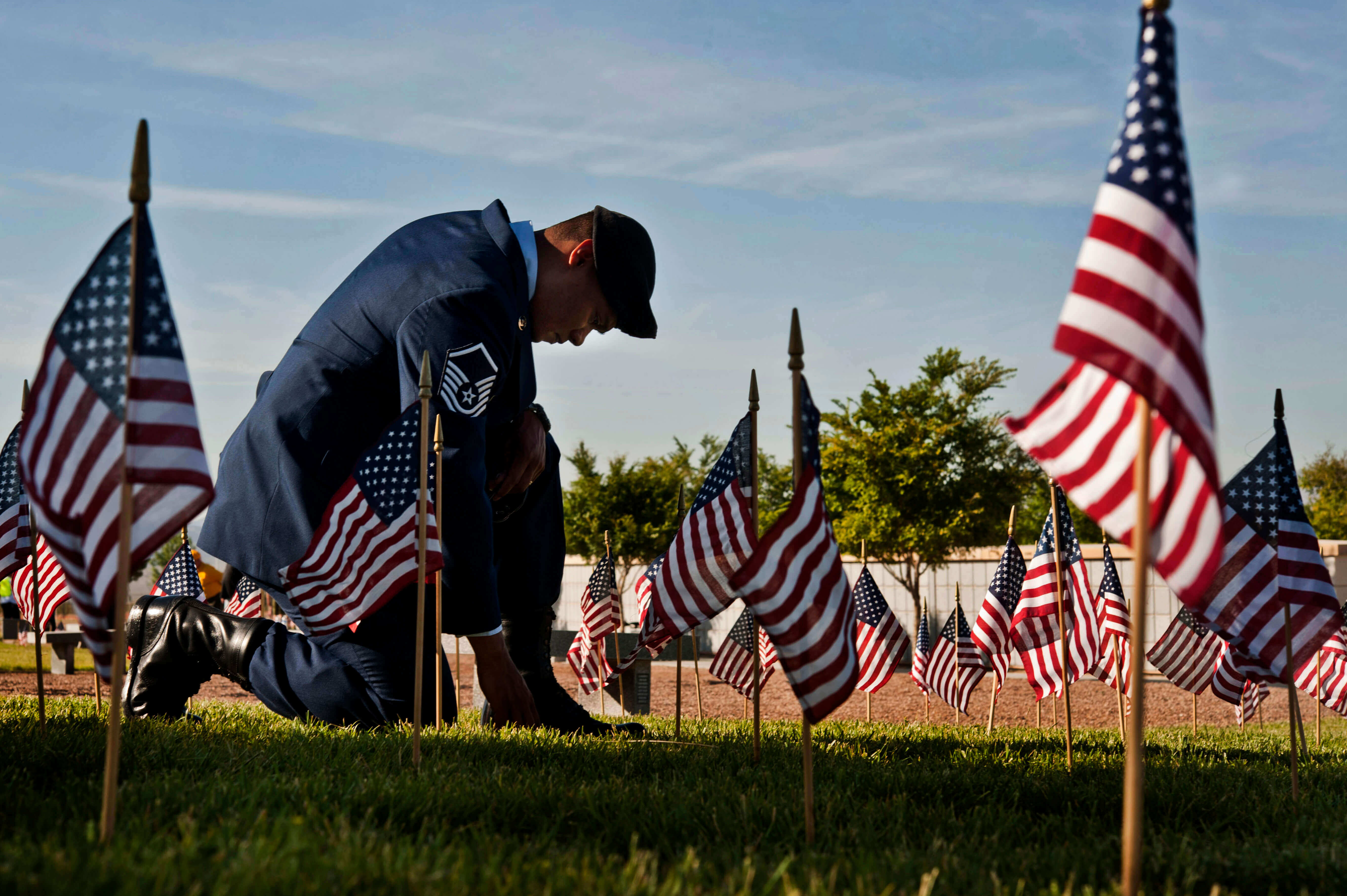Independence Day service member kneeling on ground, surrounded by small flags