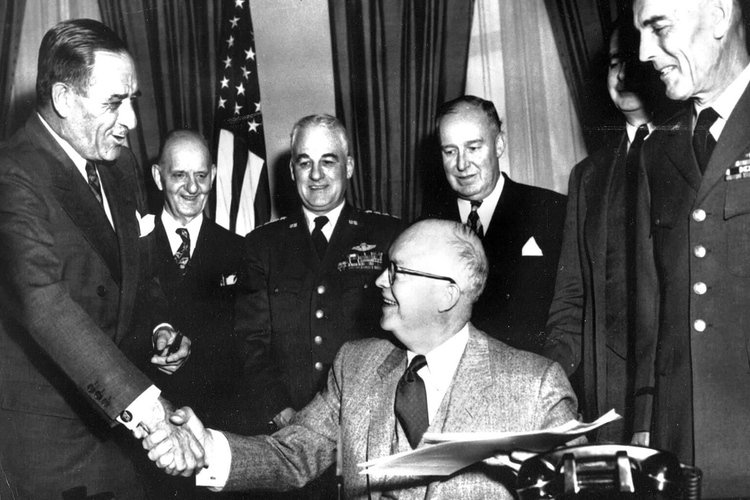 President Dwight D. Eisenhower shakes hands with Secretary of the Air Force Harold Talbott after signing legislation authorizing the establishment of the U.S. Air Force Academy.