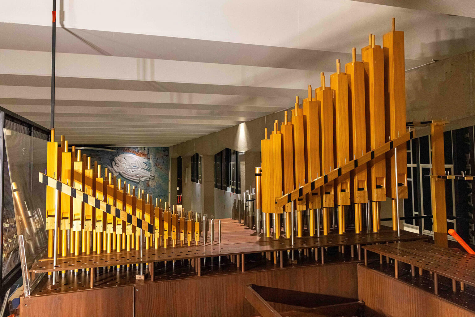 Organ components in the Catholic Chapel are reinstalled at the Cadet Chapel, U.S. Air Force Academy, Colo. on July 15, 2025. The chapel's abstract glass mosaic mural is visible in the background; its figures are crafted from Carrara marble, the same Italian stone used in world-famous sculptures such as Michelangelo's David and Pietà. (U.S. Air Force photo by Trevor Cokley)