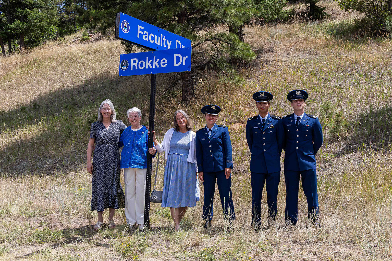 From left-to-right: Lisa Belt, daughter of retired U.S. Air Force Lt. Gen. Ervin J. Rokke; Pam Rokke, his wife; Susan Rokke, his daughter-in-law; and three cadets pose beneath the Rokke Drive sign at the U.S. Air Force Academy, Colo., July 24, 2026. Academy officials dedicated the road to Rokke, a 1962 graduate and the first Academy alumnus to serve as dean of the faculty. (U.S. Air Force photo by Trevor Cokley)
