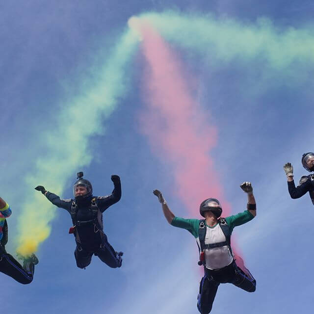 Wings of Blue members skydiving in formation with colored smoke