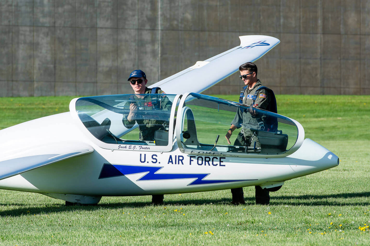 Two cadets in flight suits stand near a U.S. Air Force glider on Stillman Field. Both cadets stand beside the aircraft, both wearing sunglasses and looking towards the left. Two cadets in flight suits stand near a U.S. Air Force glider on Stillman Field. Both cadets stand beside the aircraft, both wearing sunglasses and looking towards the left.