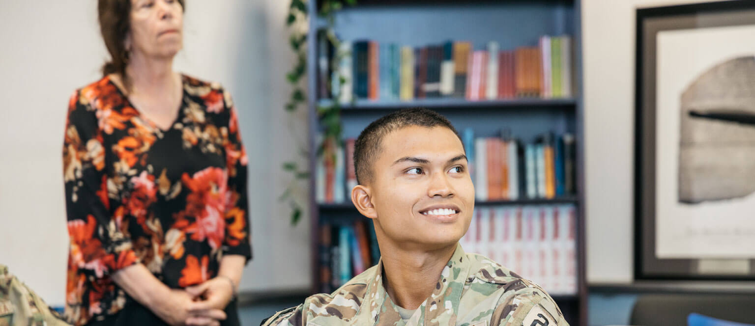 A cadet seated in a classroom among several other individuals, engaged in a learning environment.