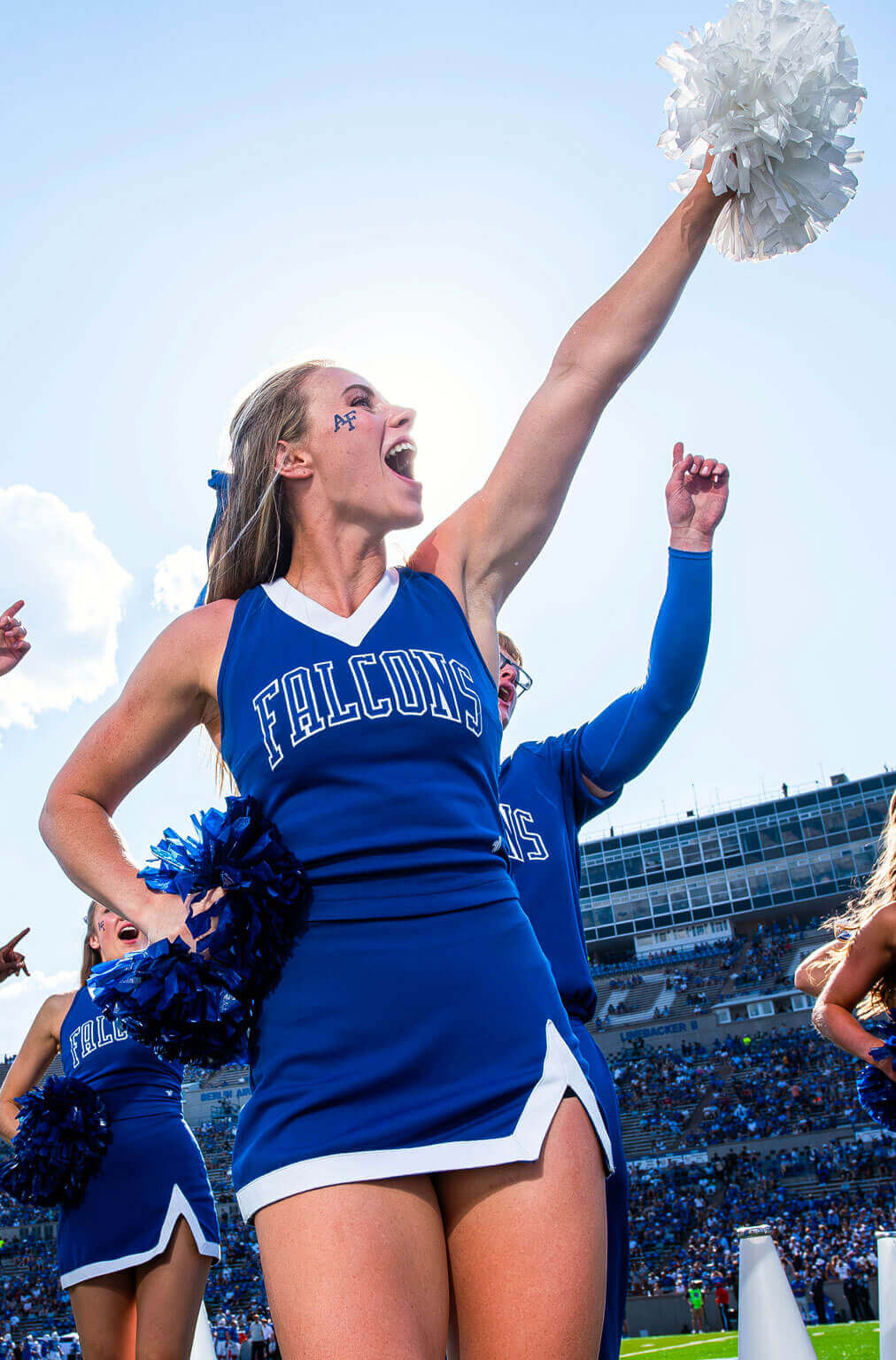 A Falcon cheerleader holding blue and white pom poms during a U.S. Air Force Academy football game. A Falcon cheerleader holding blue and white pom poms during a U.S. Air Force Academy football game.