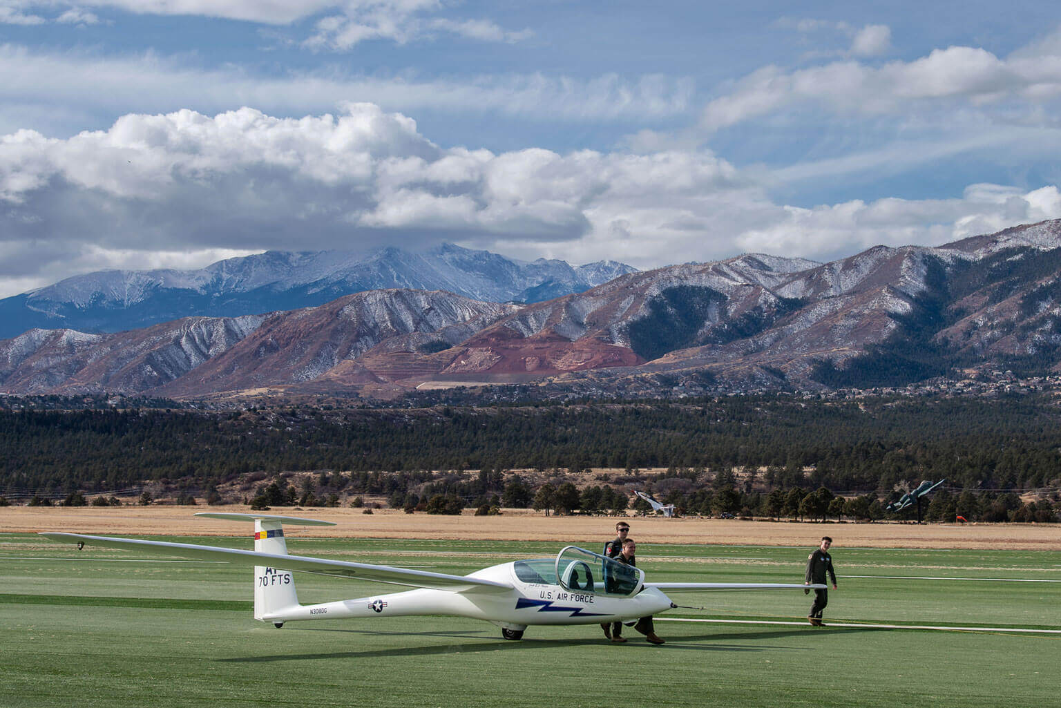 Cadets handling a glider during a soaring course at the U.S. Air Force Academy with mountains in the background.