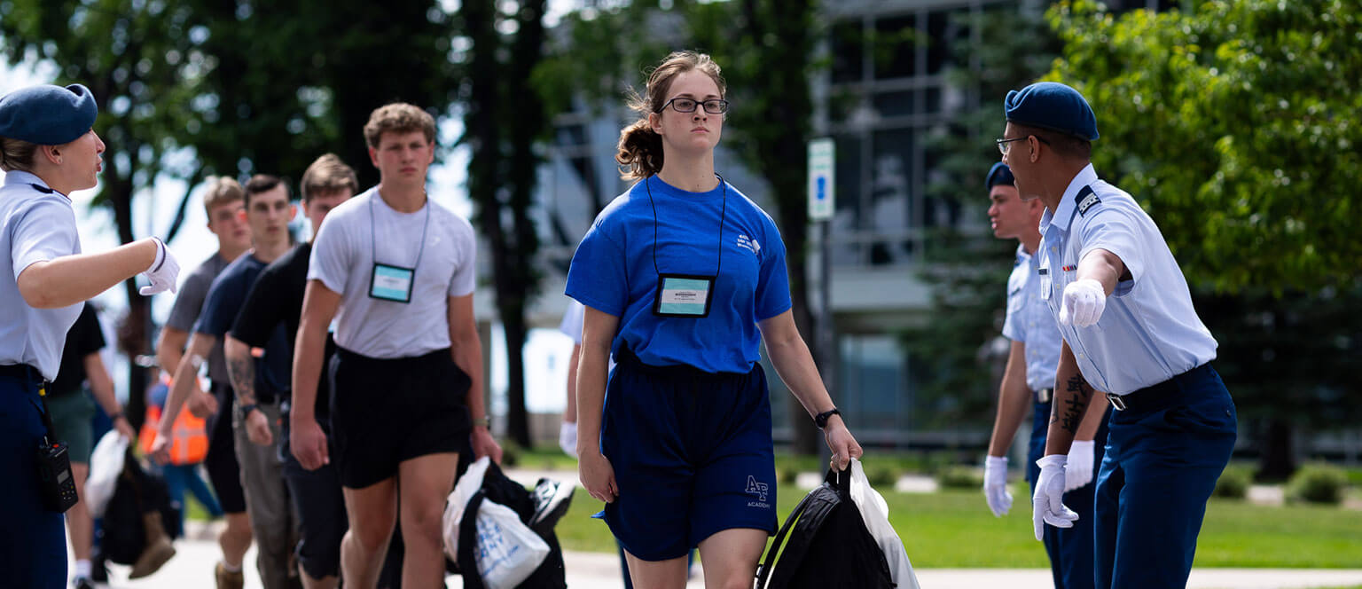 A group of appointees in athletic attire walks in formation outside. Two cadet cadre guide them, creating a disciplined atmosphere.