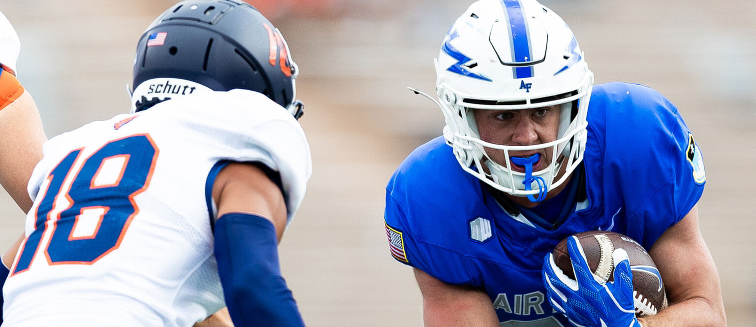 A U.S. Air Force Academy football player sprinting down the field while gripping the ball tightly in his hands.