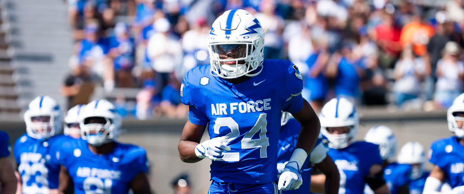 U.S. Air Force Academy football player in blue uniform running on the field during a game.