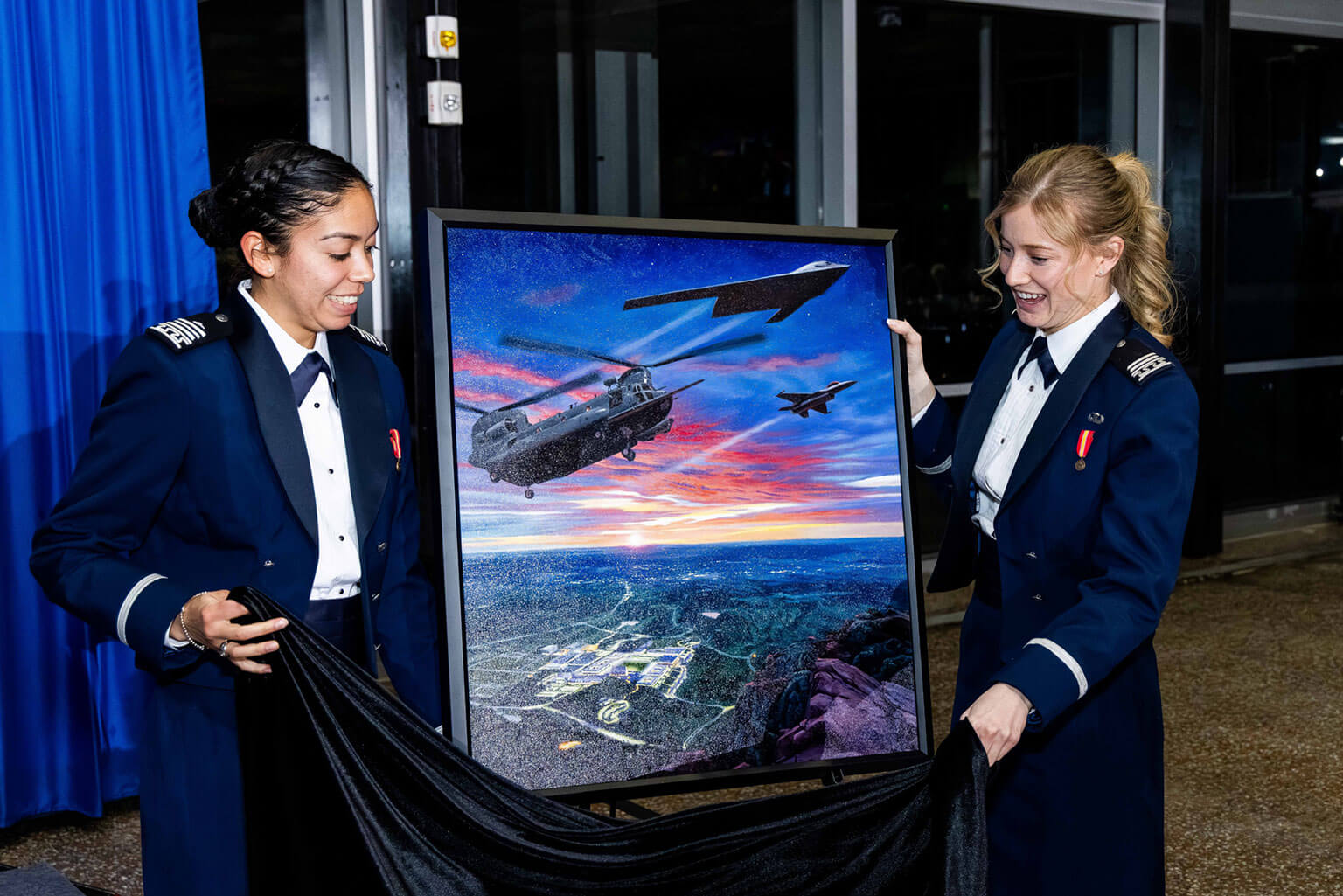 Cadets 1st Class Jocelynn Stevenson and Caroline Friedrick unveil the official painting during the Class of 2026 100s Night dining-in ceremony at Mitchell Hall, U.S. Air Force Academy, Colorado, Feb. 12, 2026. The presentation of class paintings has been a tradition for over 50 years. (U.S. Air Force photo by Trevor Cokley)