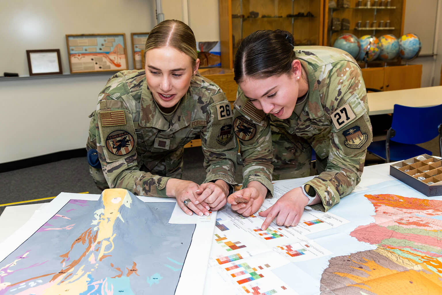 Cadet 1st Class Lauren Mirande, left, and Cadet 2nd Class Abigail Anderson, right, learn about volcanic rock types in the Geospatial Science Laboratory, at the U.S. Air Force Academy, Colo., March 19, 2026. Mirande and Anderson are learning to interpret and analyze data for future operations. (U.S. Air Force photo by Trevor Cokley)