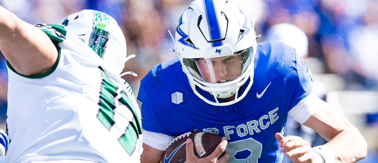 A U.S. Air Force Academy football player sprinting down the field while gripping the ball tightly in his hands.