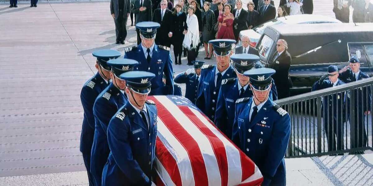 Cadet Honor Guard carrying flag-draped casket up stairs at funeral
