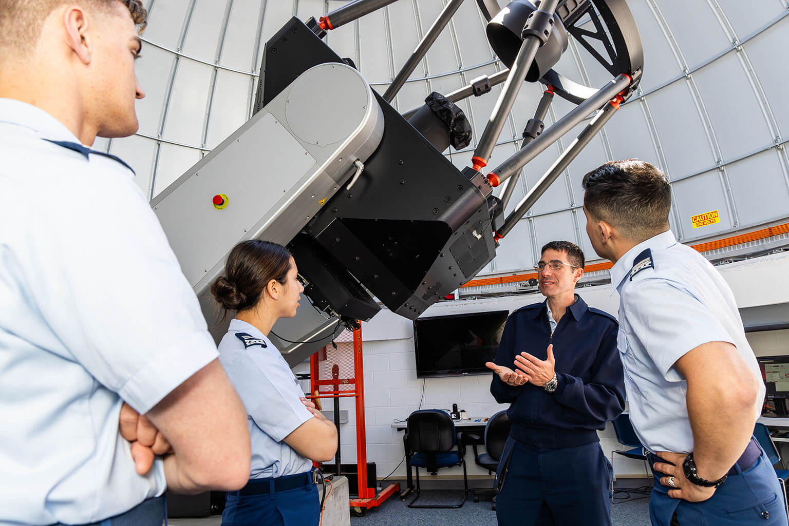 U.S. Air Force Lt. Col. Benjamin Roth briefs Cadet 2nd Class Piper Davenport, Cadet 1st Class Matthew Sharkey and Cadet 4th Class Jacob Smith on the U.S. Air Force Academy Observatory telescopes.