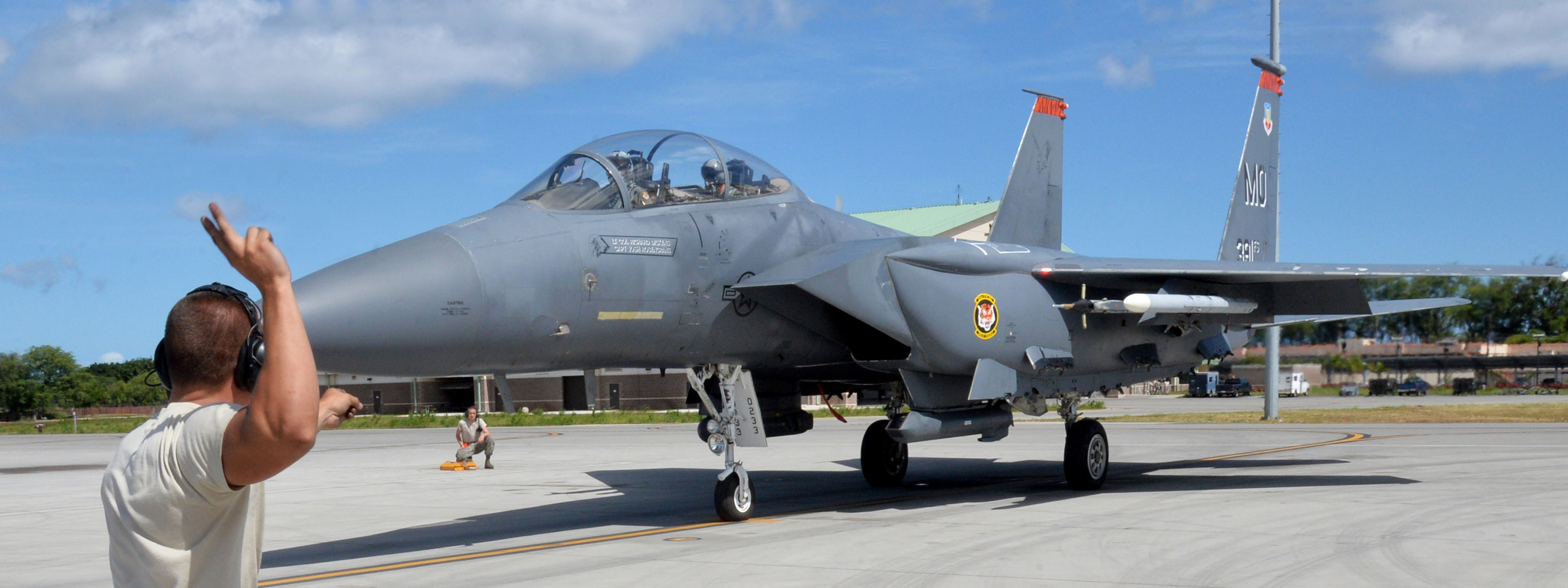A man stands on the tarmac, waving at a fighter jet, capturing a moment of interaction between people and aircraft.