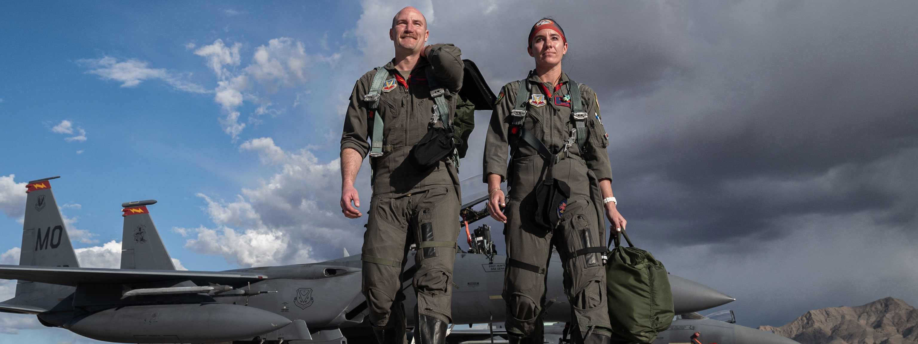 Two pilots are photographed in front of an F-15 fighter jet, highlighting their camaraderie and the aircraft's sleek profile.