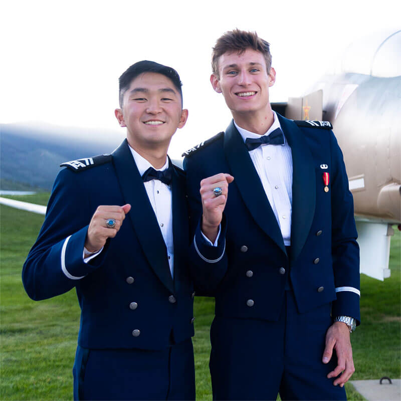 Two male cadets revealing their class rings.