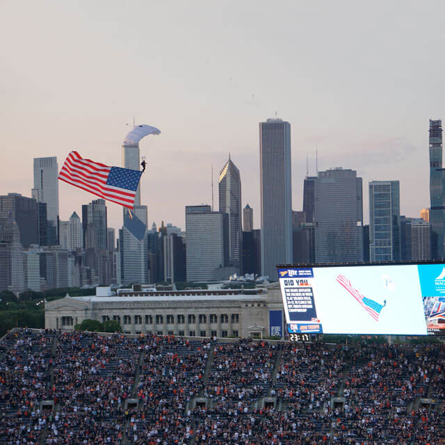 Wings of Blue member trailing flag descending into Soldier Field in Chicago