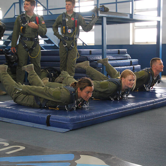 Cadets practicing skydiving form on mat.