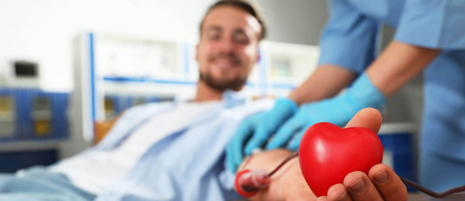 A man gently holds a vibrant red heart in his hand, while giving a blood donation.
