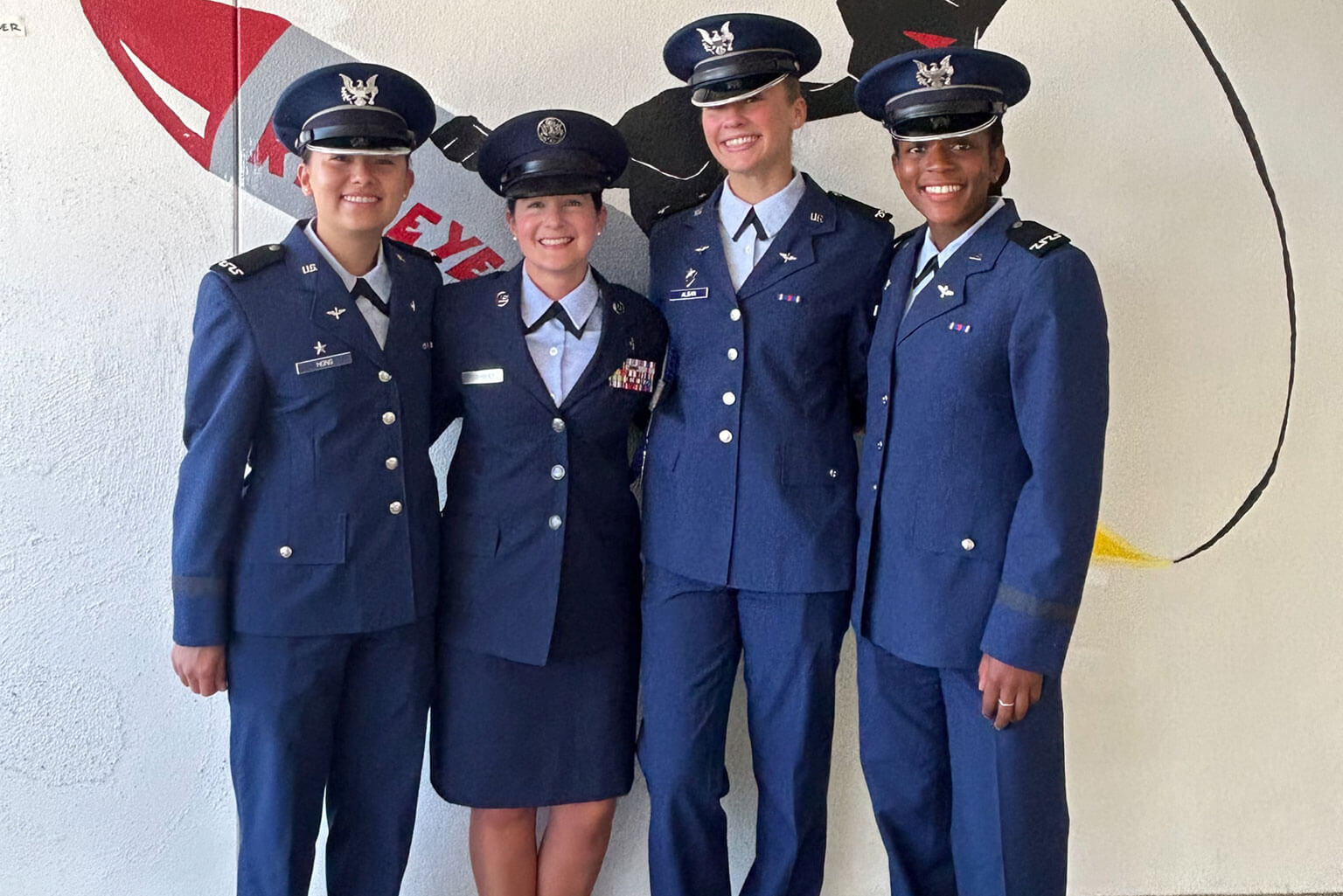Cadet 3rd Class Keilani Hong, Master Sgt. Leona Rodriguez, Cadet 3rd Class Sophia Alban and Cadet 3rd Class Ryan McFadden pose in front of a Squadron 25 mural.
