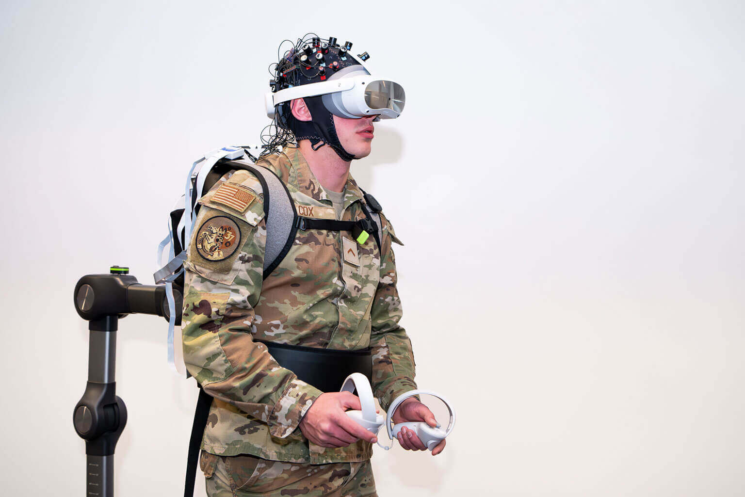 A cadet wears a VR headset with sensors and holds controllers, participating in a virtual reality training exercise.