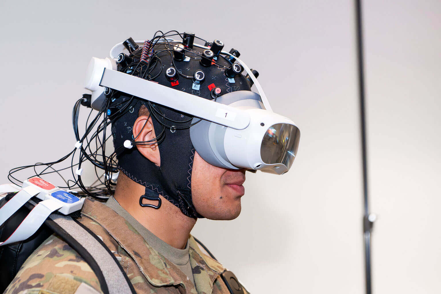 A cadet wearing a VR headset and a sensor-laden cap with wires. They are dressed in a military uniform, conveying a tech-focused atmosphere.