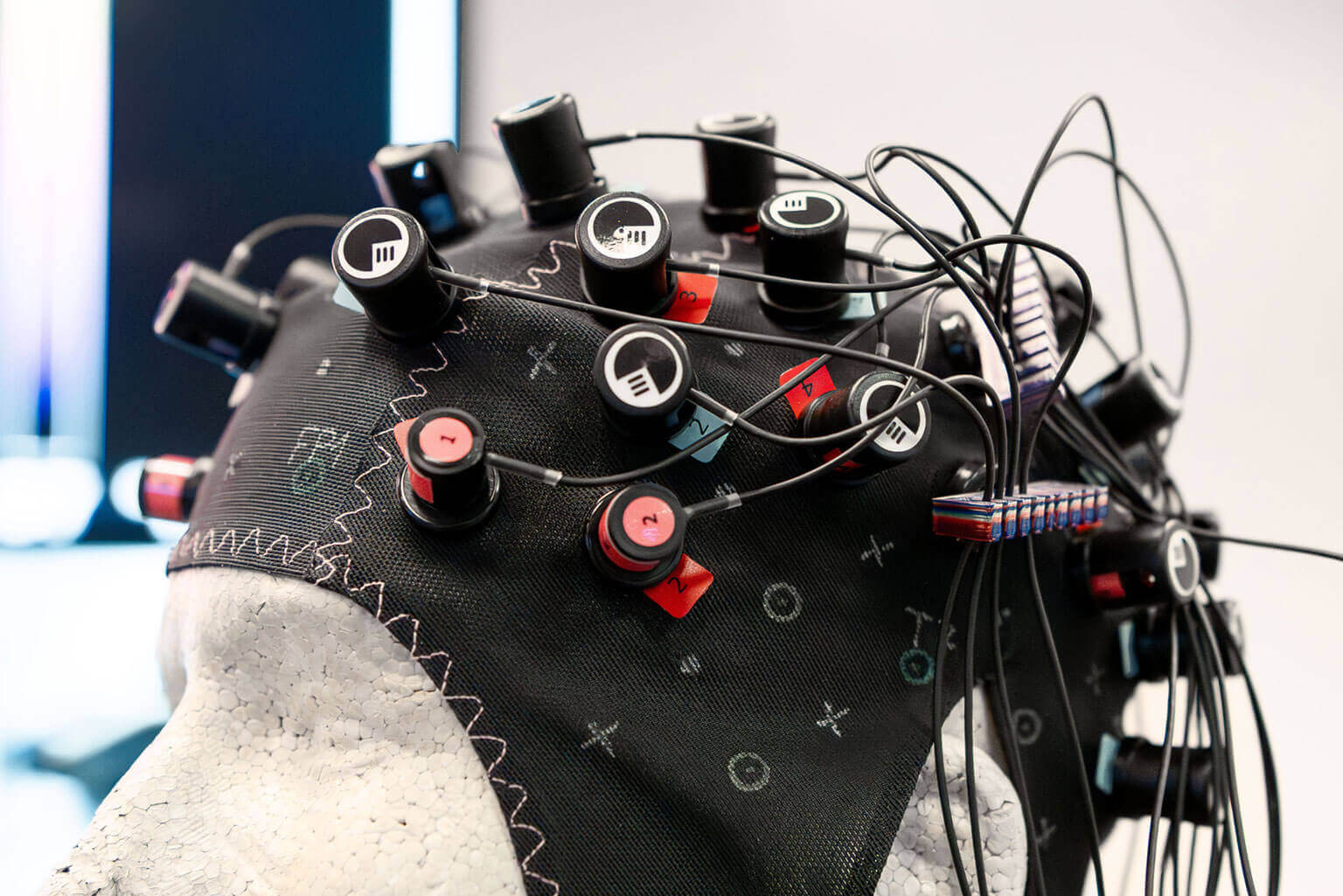 Close-up of a mannequin head wearing an EEG cap with sensors and wires for brainwave monitoring. The scene conveys a high-tech, scientific feel.