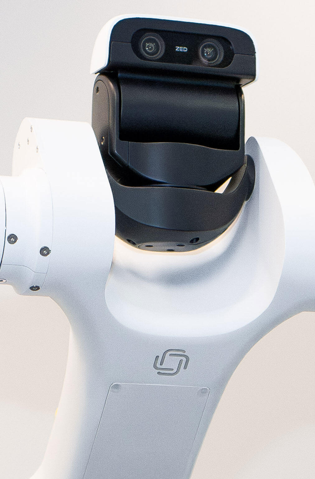 A white robot with a black camera head featuring dual lenses labeled "ZED." Sleek design and neutral background convey a modern, technological feel.